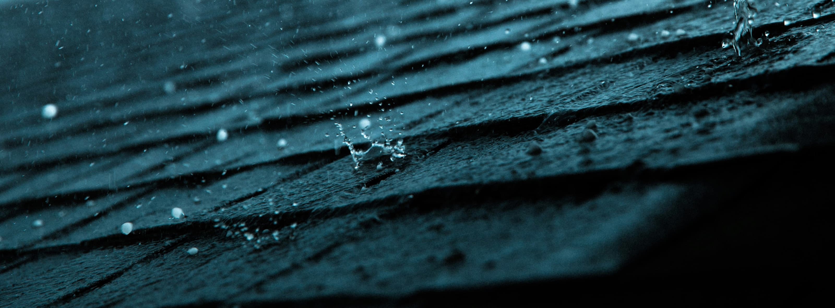 Close-up of raindrops on dark asphalt shingles