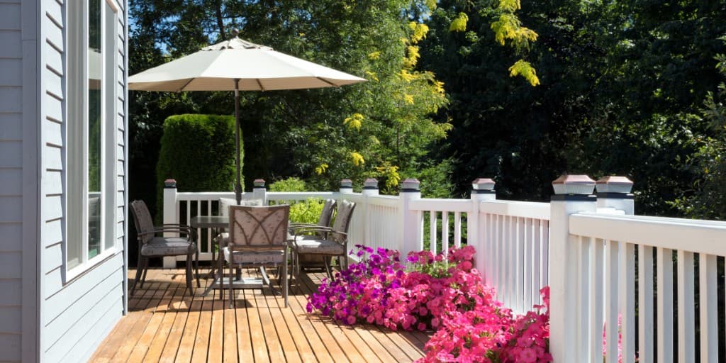 Wood deck with a white railing, patio seating, and pink flowers beside a house
