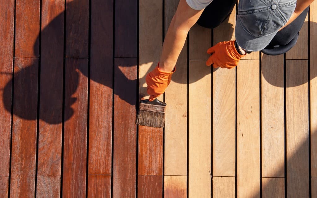 Applying brown stain to wooden deck boards.