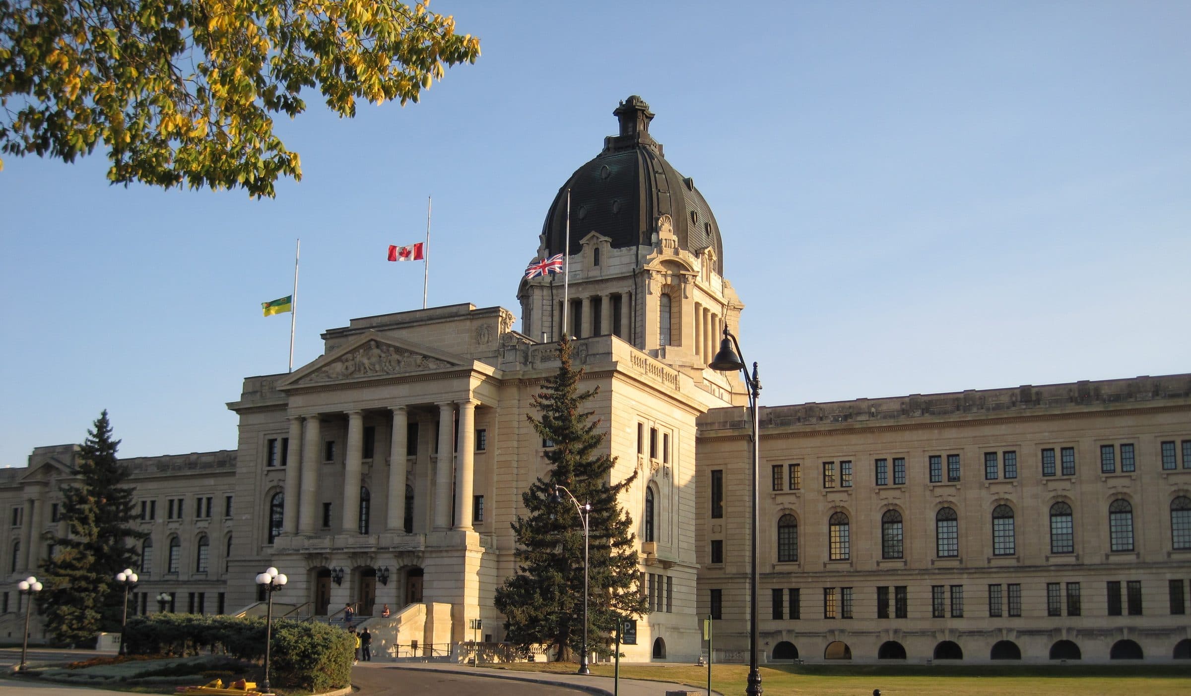 Saskatchewan Legislative Building, a stone government building with columns, a dome, and a Canadian flag, set on a green lawn under a blue sky