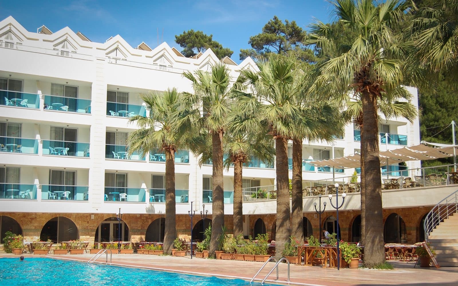 Multi-story white hotel facade with glass-railed balconies above a pool terrace