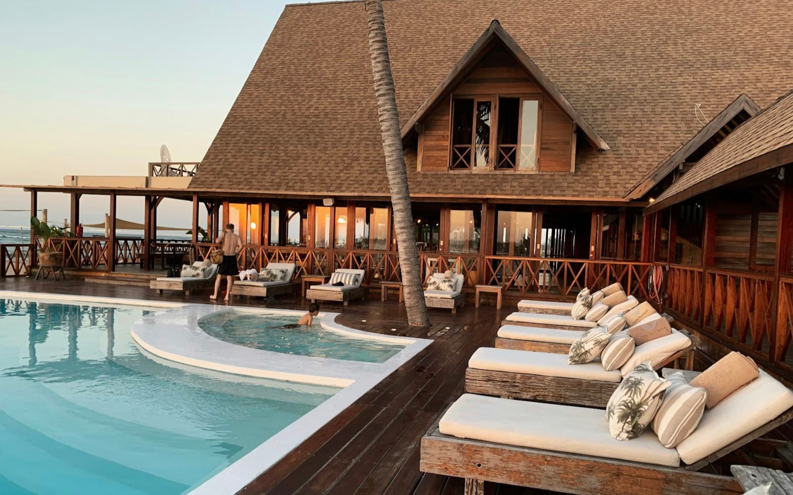 Resort lodge with a large multi-gabled shingle roof overlooking a pool deck at dusk