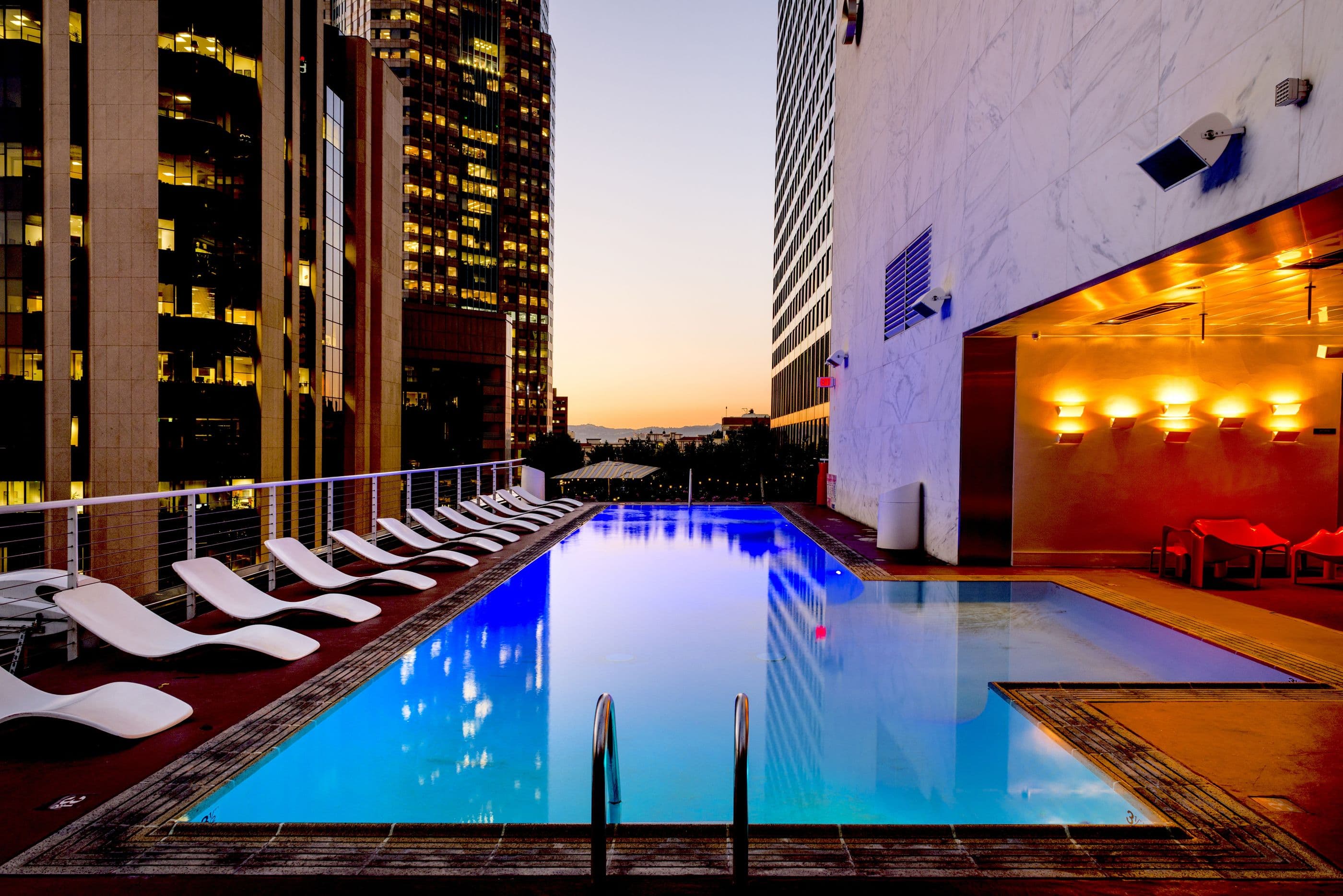 Luxury resort lodge with an illuminated pool and lounge chairs at dusk