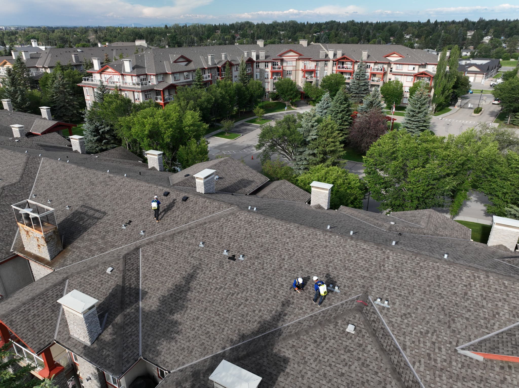 Aerial view of a multifamily residential complex with asphalt shingle roofs, balconies, and trees