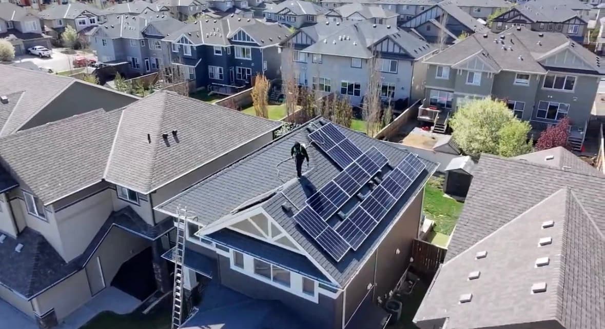 Technician spraying a residential asphalt roof beside rooftop solar panels