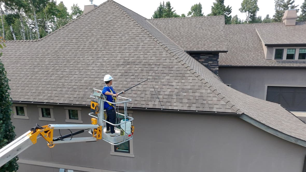 Technician on a lift spraying a steep asphalt shingle roof