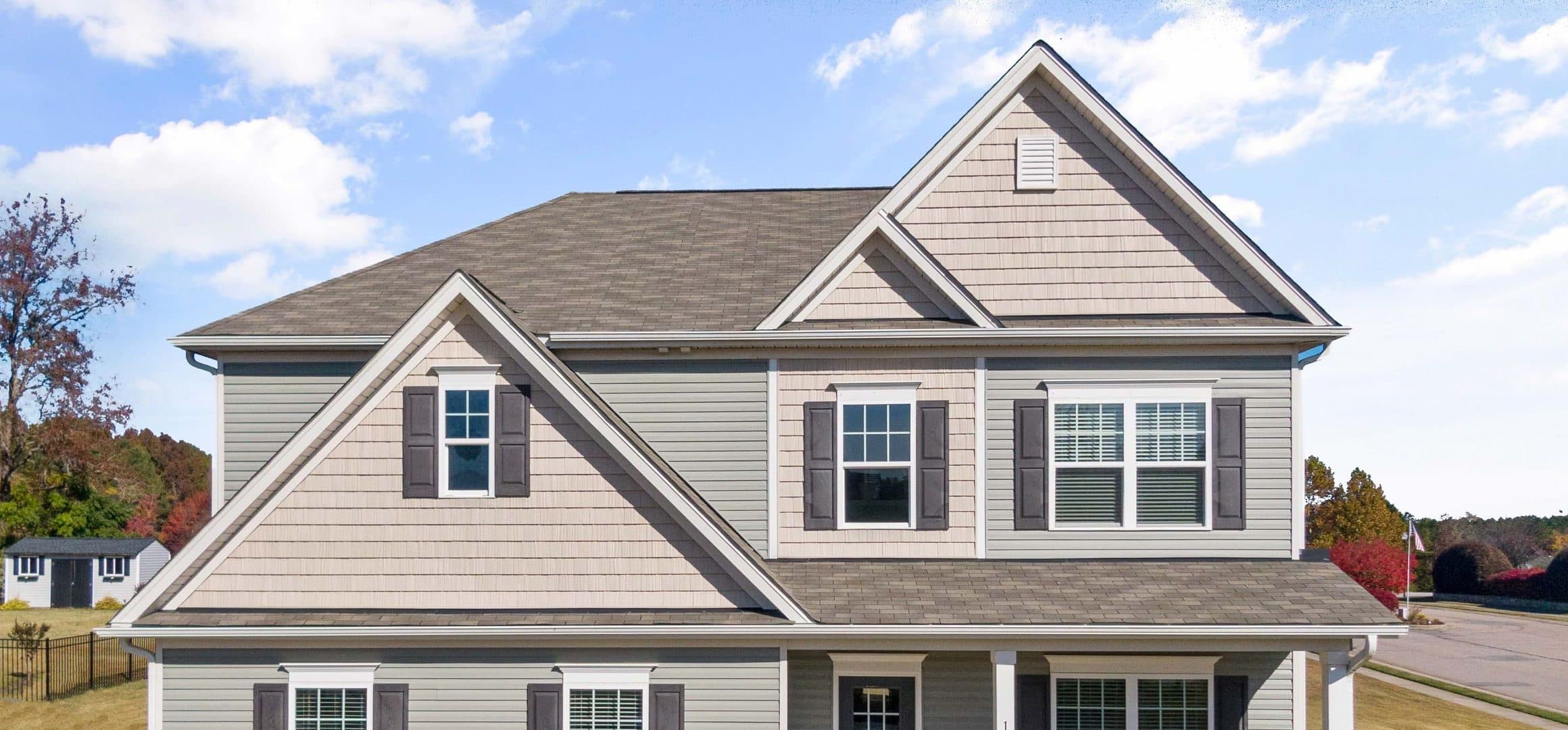 Gray suburban home with a gabled asphalt shingle roof under a blue sky