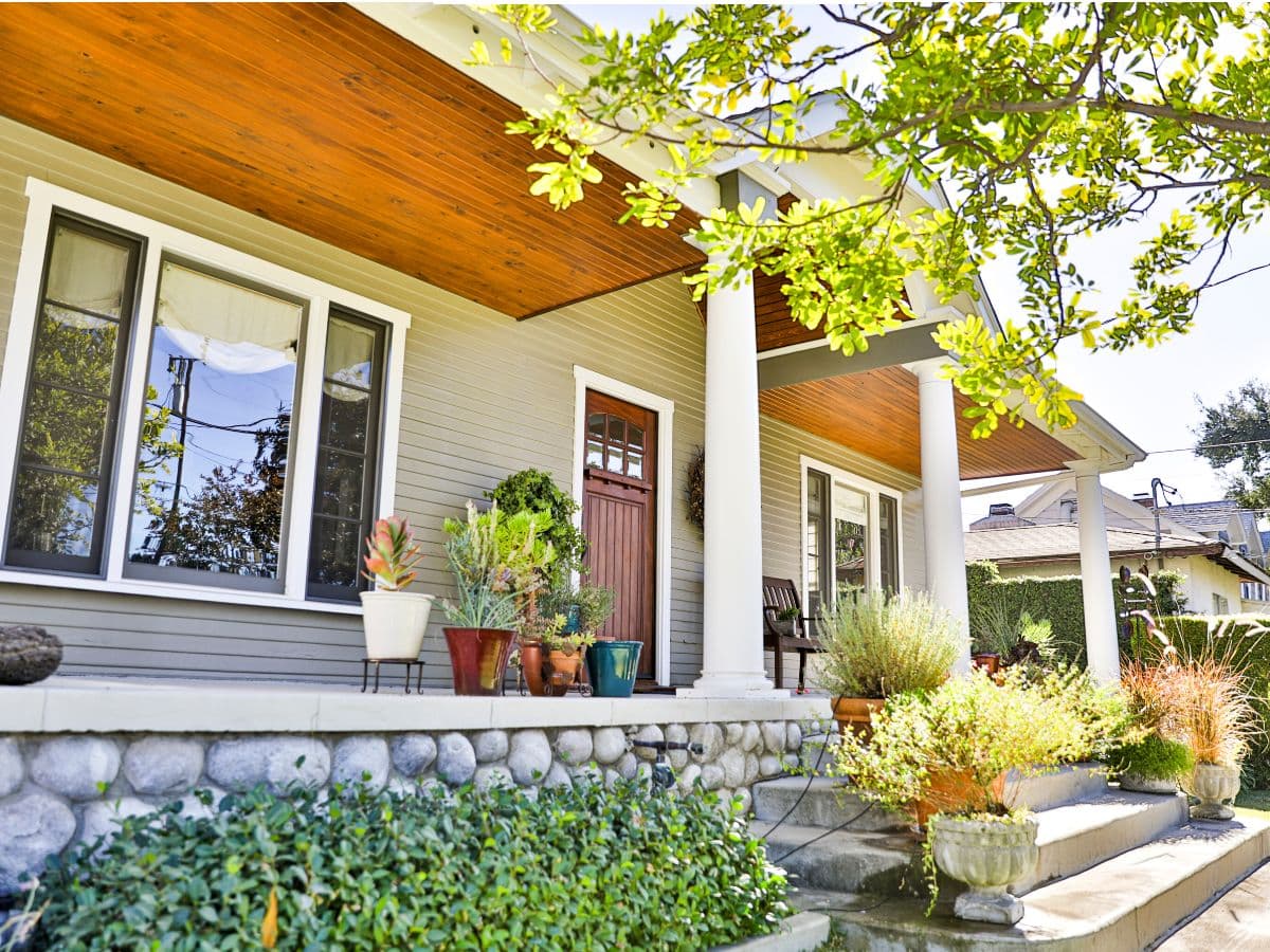 Home exterior with wood porch ceiling, siding, stonework, and landscaping.