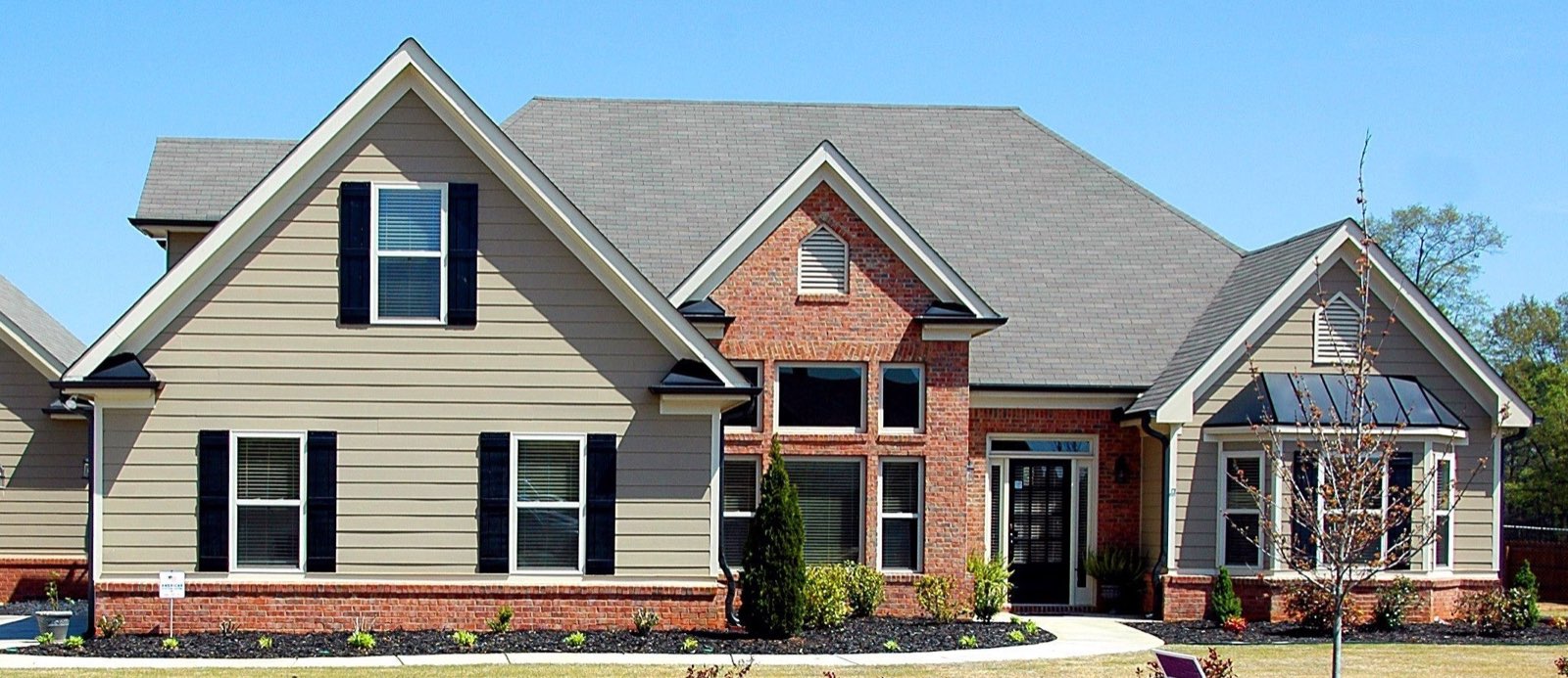 Neutral gray two-story home with a dark gray asphalt shingle roof, multiple gabled peaks, brick accents, and dark shutters